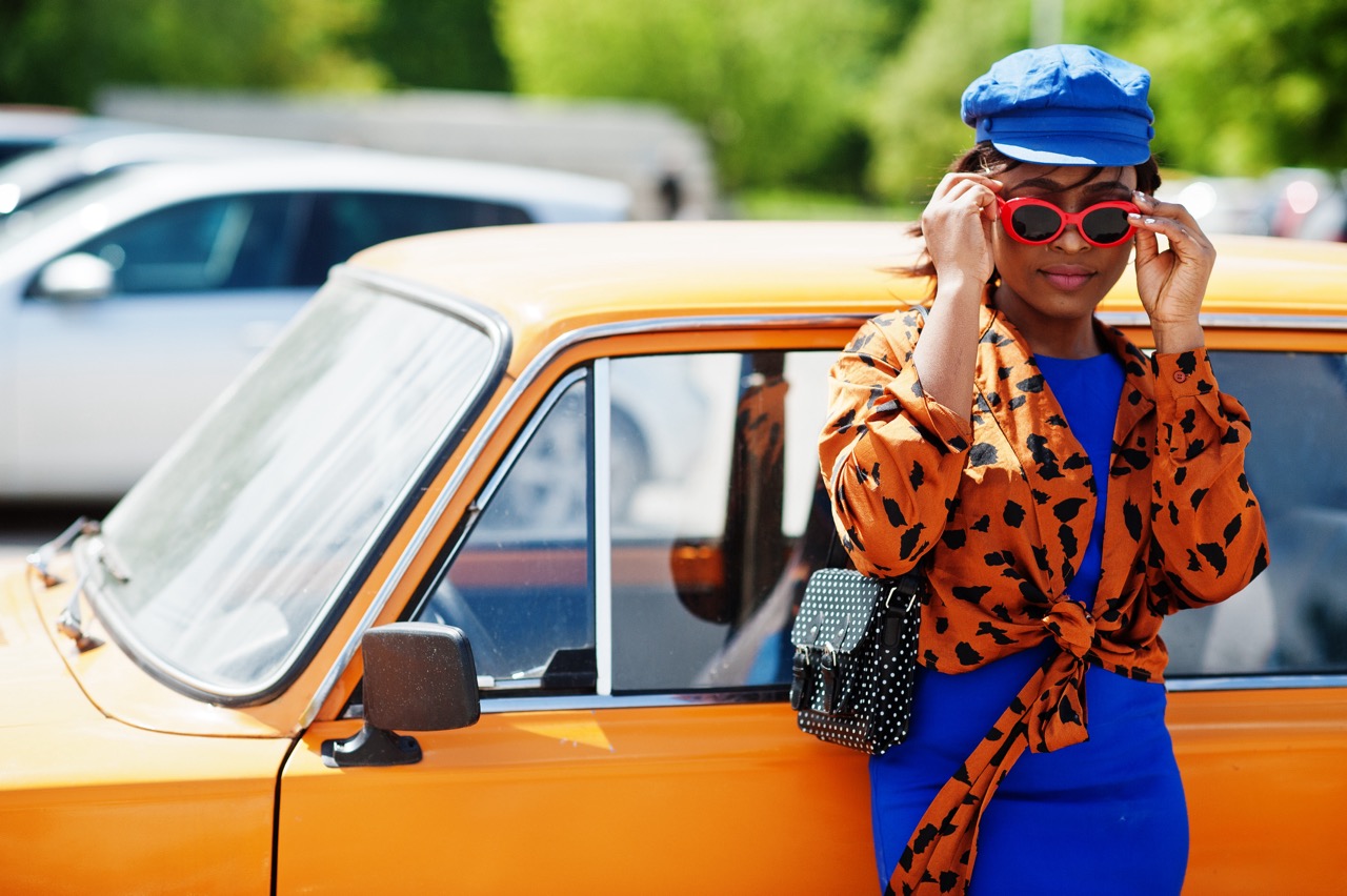 Young woman with sunglasses standing next to orange classic car